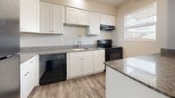This single-floor, 2-bedroom, 2-bathroom residence offers a clean, modern aesthetic defined by neutral tones, wood-style luxury vinyl flooring, and plush carpeting in the bedrooms. The open living area greets residents at the entry with a large window that brings in generous natural light and views of the surrounding exterior. The space flows seamlessly into the kitchen, which is outfitted with white shaker-style cabinetry, granite countertops, a kitchen island with matching granite surface, black appliances including a dishwasher and electric range, and a undermount sink with a modern pull-down faucet. Wood-style flooring continues throughout the main living and kitchen areas, enhancing the cohesive design.

Both bedrooms feature soft carpeting, neutral wall tones, and windows with blinds that allow for natural light and privacy. One bedroom includes access to an en-suite bathroom and walk-in closet. The two bathrooms are finished consistently with wood-style flooring, white vanities, and granite countertops. One bathroom features a soaking tub with shower combination, while the second offers a dedicated walk-in shower. The overall ambiance is clean, bright, and move-in ready.
