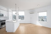 This well-designed single-floor residence offers a clean, contemporary aesthetic throughout, characterized by crisp white walls, light hardwood-style flooring, and an abundance of natural light. The open-concept layout seamlessly connects the kitchen and living area, creating a generous and airy communal space. Multiple windows frame views of the surrounding neighborhood and treeline, filling the interior with daylight.

The kitchen is a standout feature, centered around a large island with an undermount sink, pendant lighting overhead, and stone countertops. White shaker-style cabinetry extends floor to ceiling along the walls, complemented by a classic subway tile backsplash and stainless steel appliances, including a refrigerator, electric range, and over-the-range microwave. A wall-mounted mini-split unit provides climate control to the living area.

The living room is open and bright, with multiple windows offering elevated views of the surrounding urban and natural landscape, and light wood-tone flooring that carries throughout the main living spaces.

The bedroom is generously proportioned, featuring plush carpet, large windows with ample natural light and views, a ceiling fan, and the convenience of two separate closets. The bathroom is finished with a stone-topped vanity, white cabinetry, a full-width mirror, and polished chrome fixtures, presenting a clean and functional design.