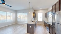 This well-appointed 2-bedroom, 2-bathroom single-story residence features a thoughtfully designed open floor plan that maximizes comfort and functionality. Light-toned hardwood-style flooring flows seamlessly through the main living areas, creating a bright and cohesive aesthetic.

The combined kitchen and living area serves as the heart of the home. The kitchen is outfitted with dark espresso cabinetry, granite countertops, a subway tile backsplash, stainless steel appliances — including a refrigerator, range, and microwave — and a center island with a sink and pendant lighting above. Large windows in the adjacent living area flood the space with natural light and provide outdoor views.

The primary bedroom is generously sized, featuring a ceiling fan, large windows, and direct access to a spacious walk-in closet with wire shelving and carpeted flooring. The second bedroom is also carpeted and includes a standard closet with built-in rods. Both bathrooms are finished with granite-top vanities, dark cabinetry, tile flooring, and a shower/tub combination.

A connecting hallway links all rooms efficiently, and the overall design is characterized by neutral tones, clean lines, and modern fixtures throughout.