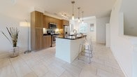 This well-designed 3-floor residence offers a thoughtfully laid-out living experience across multiple levels. The ground floor features a spacious garage with a concrete floor, housing the water heater and washer/dryer units, providing practical utility alongside convenient in-unit laundry access.

The main living level showcases a bright, open-concept floor plan anchored by a modern kitchen. Warm wood cabinetry pairs elegantly with dark granite countertops and a full suite of stainless steel appliances, including a gas range, microwave, and refrigerator. A central island with pendant lighting and bar seating serves as a focal point, flowing seamlessly into the dining area, which benefits from generous natural light through large windows with plantation shutters. The adjacent living room is equally well-lit, featuring light-toned large-format tile flooring throughout and a welcoming sectional seating area.

The upper floor is home to the bedrooms, each finished with plush carpeting and ample natural light. The bedrooms include walk-in closets with built-in shelving. The bathrooms are finished with light stone-look tile flooring and feature clean, contemporary fixtures. One bathroom offers a wood-vanity with granite countertop and vanity mirror, while another includes a glass-enclosed walk-in shower with floor-to-ceiling tile surround. Throughout, the space maintains a clean, neutral palette that lends a bright and modern ambiance.