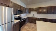 Located at 3700 42nd St S in Fargo, North Dakota, this single-floor unit offers a thoughtfully designed layout that balances functionality and modern style. The kitchen serves as a standout centerpiece, showcasing rich dark-stained cabinetry, light speckled quartz countertops, and a full suite of stainless steel appliances including a refrigerator, electric range, over-the-range microwave, and dishwasher. A spacious center island with a matching quartz surface provides additional prep space and is illuminated by a pair of elegant glass pendant lights. Light wood-tone laminate flooring runs throughout the main living and kitchen areas, lending warmth and cohesion to the space. The open-concept living area is bright and generously proportioned, featuring a sliding glass door that opens to a private balcony, allowing natural light to flow freely into the room. A baseboard heating unit ensures comfort during Fargo's colder months. The bathroom is finished with consistent dark cabinetry, a quartz vanity top, a matte black faucet and accessories, and a soaking tub and shower combination. An in-unit laundry area adds everyday convenience. The overall aesthetic is clean and contemporary, with neutral tones and quality finishes throughout.