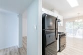 This single-floor unit features a bright, clean design highlighted by light wood-tone flooring that runs consistently throughout. The galley-style kitchen is well-appointed with white shaker cabinetry, black hardware, granite-style countertops, white subway tile backsplash, a stainless steel sink, and black appliances including a gas range and refrigerator. A skylight-style fixture illuminates the kitchen, which connects directly to the dining area. The dining space benefits from natural light through vertical blind-covered sliding glass doors and is accented by a modest chandelier overhead. The living areas are generously proportioned, each featuring ceiling fans and windows that invite natural light. Bedrooms are finished with the same wood-tone flooring and include walk-in closet access with built-in shelving. The bathroom is thoughtfully finished with large-format tile surrounding a soaking tub and sliding glass shower enclosure, complemented by a decorative mosaic accent strip, a white vanity with framed mirror, and brushed nickel fixtures. The overall aesthetic throughout is neutral, clean, and move-in ready.