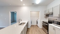 This single-floor, 2-bedroom, 2-bathroom residence in Arden, NC offers a well-designed layout with modern finishes throughout. The open-concept living area features wood-look flooring, a ceiling fan, and French doors that invite natural light while providing outdoor access. Neutral-toned walls create a clean, cohesive aesthetic across the space.

The kitchen serves as a functional centerpiece, anchored by a peninsula island with an undermount sink and white quartz countertops. Gray shaker-style cabinetry, stainless steel appliances — including a gas range, built-in microwave, and refrigerator — and recessed lighting complete the space. A dedicated laundry area with a washer is conveniently accessible directly from the kitchen.

Both bedrooms feature plush carpeting, natural light from windows, and access to closets with built-in shelving. One bathroom includes an accessible tub-shower combination with grab bars, a handheld showerhead, a fold-down bench, and a single vanity with quartz countertop. The second bathroom mirrors this design with a standard tub-shower and similar finishes, maintaining consistency throughout the home.