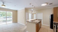 This thoughtfully laid-out one-bedroom, one-bathroom residence offers a comfortable and functional living environment across a single floor. The open-concept design connects the kitchen and living area seamlessly, creating an inviting, cohesive space.

The kitchen serves as a central hub, featuring a peninsula island with granite countertops, warm wood cabinetry, and a full suite of stainless steel appliances including a refrigerator, range, and built-in microwave. Stylish pendant lighting hangs above the island, adding a modern touch. A stacked washer and dryer unit is conveniently tucked nearby, adding in-unit laundry functionality.

The living area is finished with soft carpeting and neutral beige walls adorned with crown molding, lending a clean and classic aesthetic. Sliding glass doors open to a private balcony overlooking a lush, tree-lined outdoor setting, filling the space with natural light.

The bedroom is a well-proportioned retreat with plush carpet, double closet doors providing ample storage, and a calm, neutral color palette. The bathroom includes a single vanity with a wide mirror, wood cabinetry, tile flooring, and a full bathtub with safety grab bars. Throughout, crown molding and consistent warm tones create a cohesive and comfortable ambiance.