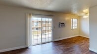 Located at 1240 Monument Blvd in Concord, California, this single-floor unit offers a straightforward and functional layout designed for comfortable everyday living. The entry foyer welcomes residents through a paneled white door topped with a fan-shaped transom window, allowing natural light to filter into the entryway, which features rich, dark wood-look flooring that extends throughout much of the unit.

The living area is generously sized and bright, highlighted by a large sliding glass door that opens to a private balcony and provides views of the surrounding community. A wall-mounted air conditioning unit ensures year-round comfort, and an additional window further enhances natural light in the space. Textured ceilings are present throughout the main living areas, adding a subtle architectural detail.

The kitchen is efficiently arranged with warm wood cabinetry, an electric range, a refrigerator, and light stone-toned countertops. A ceiling-mounted light fixture provides functional task lighting.

The bedroom offers plush carpeting underfoot, a wide horizontal window with neighborhood views, and a textured ceiling, creating a calm and restful environment. A ceiling fan with light fixture is also present in an adjacent area, adding to overall comfort.

The bathroom is well-appointed with a combination tub and shower enclosed by sliding glass doors, a wood-framed vanity mirror, white countertop, and matching wood cabinetry, all complemented by wood-look flooring.