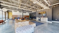 Located at 223 E Town St in the heart of Columbus, Ohio, this single-floor amenity space combines industrial-modern design with a warm, inviting atmosphere. The open-concept layout is anchored by polished concrete floors that reflect the abundant natural light streaming in through expansive floor-to-ceiling windows, offering views of the surrounding urban streetscape.

The main lounge area is a standout, featuring tufted leather sectional sofas, eclectic accent chairs, and vibrant throw pillows in teal, mustard, and orange. A warm wood accent wall provides a rich textural contrast against the deep charcoal-painted walls. Overhead, exposed steel ceiling trusses are draped with strands of Edison bulb string lights, complemented by dramatic globe pendant chandeliers that lend an elegant yet industrial character to the space.

A built-in kitchenette with white cabinetry, a beverage refrigerator, and a wall-mounted display screen serves as a functional hub within the lounge. A dedicated fitness center, separated from the lounge, is outfitted with treadmills, ellipticals, a cable machine, and a full rack of accessories, all beneath drum pendant lights and beside large windows that keep the room bright and energizing. The space as a whole delivers a sophisticated, community-focused environment ideal for both relaxation and active use.
