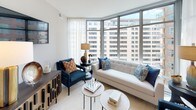 Located at 4850 Rugby Ave, Unit 1004 in the heart of Bethesda, Maryland, this contemporary residence offers a thoughtfully designed single-floor layout with refined finishes throughout. The open-concept kitchen is a standout feature, showcasing marble-veined quartz countertops, sleek white cabinetry contrasted by dark upper cabinets, an undermount sink with a brushed gold faucet, and a full suite of stainless steel appliances. Light wood-style flooring flows seamlessly from the kitchen into the adjoining dining and living areas. The living room is bathed in natural light through expansive floor-to-ceiling windows that frame sweeping views of the surrounding Bethesda cityscape, creating a bright and airy atmosphere. Multiple bedrooms offer well-proportioned spaces, each with large windows that invite abundant daylight and urban views. The bathrooms are finished with large-format tile flooring, white vanities with ample storage, and clean, modern fixtures — one featuring a soaking tub with subway tile surround. Throughout the residence, a neutral palette of soft grays, warm whites, and natural wood tones establishes a calm, sophisticated ambiance. The overall design balances modern urban living with comfortable, functional spaces ideal for everyday life.