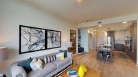 This single-story unit offers a thoughtfully designed open-concept layout that seamlessly connects the living, dining, and kitchen areas. Light wood flooring runs throughout the main living spaces, contributing to a warm, contemporary aesthetic. The living room is generously proportioned, featuring a striking accent wall with an artistic mural, a ceiling fan, and floor-to-ceiling windows that frame expansive city and treetop views. A sliding glass door opens directly onto a private balcony, further enhancing the connection to the outdoors.

The kitchen is outfitted with quartz countertops, a waterfall-edge island with bar seating, two-tone cabinetry combining white upper cabinets with dark wood lower cabinets, stainless steel appliances, a tile backsplash, and pendant lighting overhead.

The bedroom is a spacious retreat with large windows that invite abundant natural light and offer sweeping outdoor views. A sliding barn door leads directly into the bathroom, which features a long, dark-wood vanity with quartz countertops, a backlit mirror, open shelving, tile flooring, and a walk-in glass-enclosed shower with tile surround. The overall ambiance throughout is modern, bright, and cohesive.