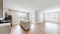 Located at 65 S. Washington Ave in Columbus, Ohio, this single-floor residence offers a well-designed, open-concept layout with contemporary finishes throughout. The kitchen serves as the heart of the home, anchored by a large center island with a white countertop, undermount sink, and pendant lighting. White shaker-style cabinetry reaches toward the ceiling, complemented by stainless steel appliances including a refrigerator, range, and microwave. Light hardwood-style flooring extends through the kitchen and living areas, enhancing the bright, airy atmosphere created by multiple windows with natural light. A wide entryway hallway with built-in storage leads smoothly into the main living spaces. The bedrooms feature plush carpeting and generously sized windows that bring in outdoor views of the surrounding neighborhood. Each bedroom is served by a dedicated walk-in closet equipped with wire shelving systems for organized storage. The bathroom includes a single-sink vanity with a framed mirror, tiled shower-tub combination, and hardwood-style flooring. Neutral wall tones and clean white trim are consistent throughout, contributing to a cohesive, modern aesthetic well-suited for comfortable everyday living in the heart of Columbus.