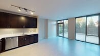This single-floor apartment in Oak Park, IL offers a contemporary open-concept design with light wood-style flooring throughout the main living areas. The kitchen features dark espresso cabinetry, stainless steel appliances, a tile backsplash, and track lighting. The spacious living area connects directly to a private patio surrounded by lush mature trees, accessible through floor-to-ceiling glass sliding doors. Carpeted bedrooms provide a cozy retreat with large windows offering outdoor views. Two full bathrooms include clean white tile, dark vanities, and tub-shower combos.