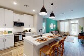 This well-designed single-floor residence offers a thoughtful layout that balances open communal spaces with private retreats. The heart of the home is an open-concept kitchen and living area, where crisp white shaker cabinets, quartz countertops, and stainless steel appliances define a modern kitchen. A peninsula with seating, illuminated by pendant lighting, connects the kitchen to the living space, which features rich wood-look flooring, a statement teal accent wall, and a door providing access to outdoor natural light. A second living or flex area showcases additional large windows, filling the space with an abundance of natural light. Both bedrooms are carpeted and feature soft mint-toned accent walls, large windows with outdoor views, and ceiling fans. The primary bedroom connects to an en-suite bathroom with a wide white vanity, matte black hardware, wood-look flooring, and a generous walk-in closet with built-in shelving. A second full bathroom mirrors the clean aesthetic with a white vanity, soaking tub, and access to an additional walk-in closet. Throughout the residence, matte black fixtures and hardware provide a cohesive, contemporary design language that ties each room together.
