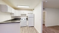 This single-floor unit offers a thoughtfully designed layout with a clean, neutral aesthetic carried throughout every room. Light wood-style flooring runs continuously across the space, lending a cohesive, modern feel. The kitchen is well-appointed with crisp white shaker cabinetry, dark countertops, a gas range, a full-size refrigerator, and a built-in sink. A peninsula-style counter creates a natural divide between the kitchen and the open living area, which is brightened by multiple windows dressed with vertical blinds. An additional area adjacent to the kitchen provides extra counter space and upper cabinet storage, ideal for a dining nook or additional prep area. The bedroom is a generously proportioned room featuring a large window that fills the space with natural light and a full-width sliding mirrored closet offering substantial storage. The bathroom is efficiently laid out with a pedestal sink, toilet, and a tiled soaking tub with a towel bar. Built-in shelving is also present near the hallway, adding practical storage. Overall, the unit presents a bright, functional, and move-in ready environment with a clean, understated design.
