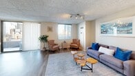 This single-floor residence offers a thoughtfully designed layout that balances comfort and functionality throughout. The open-concept living area is anchored by durable wood-look flooring, track lighting, and large windows that flood the space with natural light, while a sliding glass door leads to a private balcony overlooking the surrounding cityscape. The dining area sits adjacent to the living room, featuring the same stylish flooring and direct balcony access, creating a seamless indoor-outdoor flow. The kitchen is well-equipped with rich dark cabinetry, ample counter space, a double-basin sink, and black appliances including a range, microwave, and refrigerator. Both bedrooms are generously sized, finished with plush carpeting, and feature windows with urban views, providing a quiet and restful retreat. The primary bedroom includes convenient closet space with direct access to the full bathroom. The bathroom is cleanly appointed with wood-look flooring, a dark-stained vanity with a white countertop, and a tub-shower combination. Throughout the residence, drop tile ceilings provide a consistent aesthetic, and the neutral warm tones create a calm, cohesive ambiance well-suited to modern living.