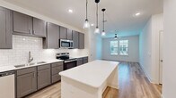 This well-appointed 2-bedroom, 2-bathroom single-story home offers a thoughtfully designed open-concept layout finished with light hardwood-style flooring throughout. The kitchen serves as the heart of the home, showcasing gray shaker cabinetry, a classic white subway tile backsplash, quartz countertops, and a full suite of stainless steel appliances including a refrigerator, range, microwave, and dishwasher. A central kitchen island with pendant lighting above provides additional prep space and a natural gathering point that flows seamlessly into the living area, which is brightened by natural light from multiple windows and equipped with a ceiling fan. Both bedrooms are comfortably sized, featuring ceiling fans, window blinds for light control, and walk-in closets with built-in shelving and hanging rods for efficient storage. The primary bedroom offers a generous footprint with an adjoining walk-in closet. The bathrooms are finished with clean, modern aesthetics, including dark-toned vanities with quartz countertops, dual sinks, brushed nickel fixtures, large mirrors, and a tiled tub-shower combination. The overall design palette of neutral tones, contemporary fixtures, and consistent flooring creates a cohesive, move-in-ready living environment.