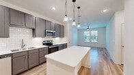 This well-appointed 2-bedroom, 2-bathroom single-story home offers a thoughtfully designed open-concept layout finished with light hardwood-style flooring throughout. The kitchen serves as the heart of the home, showcasing gray shaker cabinetry, a classic white subway tile backsplash, quartz countertops, and a full suite of stainless steel appliances including a refrigerator, range, microwave, and dishwasher. A central kitchen island with pendant lighting above provides additional prep space and a natural gathering point that flows seamlessly into the living area, which is brightened by natural light from multiple windows and equipped with a ceiling fan. Both bedrooms are comfortably sized, featuring ceiling fans, window blinds for light control, and walk-in closets with built-in shelving and hanging rods for efficient storage. The primary bedroom offers a generous footprint with an adjoining walk-in closet. The bathrooms are finished with clean, modern aesthetics, including dark-toned vanities with quartz countertops, dual sinks, brushed nickel fixtures, large mirrors, and a tiled tub-shower combination. The overall design palette of neutral tones, contemporary fixtures, and consistent flooring creates a cohesive, move-in-ready living environment.