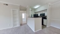 This single-story, 2-bedroom, 1-bathroom unit offers a practical and comfortable layout designed for everyday living. The open-concept kitchen and living area serves as the heart of the unit, where a peninsula with dark countertops separates the kitchen from the carpeted living space. The kitchen features white cabinetry, a tile backsplash, black appliances including a refrigerator, microwave, and range, and wood-look flooring. Crown molding and a pendant light fixture add a polished touch to the living area. A built-in shelving unit is integrated into the wall, providing convenient display or storage space.

A hallway connects the main living area to the two bedrooms and bathroom. The spacious primary bedroom features large windows that allow ample natural light, a ceiling fan, and soft carpet flooring. It is accompanied by a generously sized walk-in closet with multi-level shelving and a hanging rod. The second bedroom is equally well-proportioned, featuring crown molding and plush carpeting. The full bathroom is appointed with dark wood-look flooring, a white vanity with storage cabinetry, a large mirror, and a combined tub and shower. Neutral tones and clean finishes throughout contribute to a bright, cohesive aesthetic.