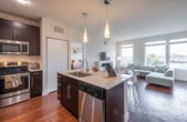 This well-appointed single-floor residence offers a thoughtfully designed open-concept layout that seamlessly connects the kitchen, dining, and living areas. The kitchen is a standout feature, boasting dark espresso cabinetry that extends to the ceiling, stone countertops, a large center island with an undermount sink, stainless steel appliances including a French door refrigerator, and elegant pendant lighting overhead. Rich hardwood flooring flows throughout the main living spaces, adding warmth and continuity.

The living room is bright and inviting, anchored by a sleek fireplace with a white surround, a wall-mounted flat-screen TV, and a ductless mini-split climate control unit. A generous bank of windows floods the space with natural light and offers expansive views of the surrounding neighborhood and beyond.

The primary bedroom features large windows framing scenic outdoor views, plush carpeting, and a ceiling fan. A second bedroom provides a comfortable, softly lit retreat with carpeted flooring. The primary bathroom is finished with large-format neutral tiles, a glass-enclosed walk-in shower, dark vanity cabinetry, and stone countertops. A second bathroom offers a full soaking tub with a tiled shower surround, ideal for relaxing. Together, these spaces create a refined, modern living environment.