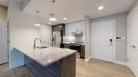 This single-floor residence features a thoughtfully designed open-concept layout that seamlessly connects the living and kitchen areas. The contemporary kitchen serves as a focal point, showcasing a large island with a granite countertop, an undermount sink, and dark wood cabinetry paired with light upper cabinets. Stainless steel appliances, including a French door refrigerator, electric range, and built-in microwave, provide a complete cooking suite. A textured penny-tile backsplash adds visual interest, while pendant lighting above the island and recessed ceiling lights ensure a well-lit workspace.

The open living area is finished with warm-toned wood-look flooring that extends throughout, complemented by neutral painted walls and clean white trim. A set of French doors allows natural light to fill the space. Adjacent to the kitchen, a dedicated closet area provides ample built-in storage.

The unit includes two bathrooms: one featuring a soaking tub and shower combination with mosaic tile accents, and a second larger bathroom equipped with a glass-enclosed walk-in shower, accessibility grab bars, and light large-format floor tiles. A walk-in closet with wire shelving provides additional organized storage.