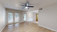This well-appointed single-floor residence offers a thoughtfully designed layout comprising one bedroom, one bathroom, a living room, and a kitchen. Light hardwood flooring runs throughout the space, lending warmth and visual continuity to every room. The living area is open and airy, featuring a ceiling fan with built-in lighting and multiple windows with blinds that allow generous natural light to filter in. A glass-paned exterior door opens to the outside, enhancing the sense of openness. Track lighting in the hallway provides additional illumination leading to the private areas of the home. The kitchen is outfitted with clean white cabinetry, speckled quartz countertops, and a stainless steel undermount sink accented by a sleek matte black pull-down faucet. The generously sized bedroom accommodates a ceiling fan, two closet doors, and a window that brings in natural light. The bathroom is a standout, featuring marble-look tile on both the floors and full tub surround, a soaking bathtub with modern fixtures, and a contemporary white vanity. Neutral wall tones throughout create a clean, cohesive aesthetic, making this a practical and modern living space.