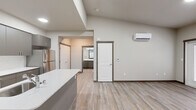 Located at 83 NE Ridge Point Blvd in Belfair, Washington, this thoughtfully designed one-bedroom, one-bathroom unit offers a clean, modern aesthetic throughout. The open-concept kitchen and living area serves as the heart of the home, showcasing vaulted ceilings that lend an airy sense of spaciousness. The kitchen is well-appointed with gray flat-panel cabinetry, white quartz countertops, a central island with an undermount sink, and a full suite of stainless steel appliances including a refrigerator, electric range, and microwave. Light wood-look luxury vinyl plank flooring runs throughout the main living areas, complementing the neutral color palette. A wall-mounted ductless mini-split unit provides efficient heating and cooling to the living space. The bedroom features soft carpeting, a window with views of the surrounding greenery, and a double-door closet offering ample storage. The bathroom includes a full soaking tub and shower combo, a vanity with white countertop, and open wire shelving for additional storage. A dedicated laundry area, balcony access with natural light, and a hallway with additional closet space round out this well-organized and modern unit.