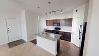 Located at 6310 S Watson Rd in Grand Prairie, Texas, this single-story residence offers a well-organized layout designed for comfortable everyday living. The kitchen serves as a central highlight, showcasing rich dark-toned cabinetry paired with granite countertops that extend across both the perimeter surfaces and a generously sized central island. The island includes an integrated sink and provides additional seating and prep space, making it a functional focal point of the open living area. A track lighting system and pendant lights overhead ensure ample illumination throughout the kitchen. Black appliances, including a range, microwave, and refrigerator, complement the cabinetry, while wood-style flooring grounds the kitchen space before transitioning to plush carpeting in the adjacent living areas.

The bedroom is a calm, neutral space featuring soft carpet, a ceiling fan with light fixture, and a window fitted with blinds that allows natural light to filter in. A spacious walk-in closet accompanies the bedroom, offering dual hanging rods and built-in shelving for organized storage.

The bathroom features dark cabinetry below a wide vanity with a white countertop and a large mirror above. Wood-style flooring, a wall-mounted towel bar, and a separate shower complete the well-appointed space. Overall, the unit presents a clean, cohesive aesthetic throughout.