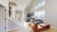 This two-story home offers a thoughtfully designed layout spread across two floors, combining modern aesthetics with functional living spaces. The main floor is anchored by an open-concept kitchen and living area that immediately impresses with its dramatic vaulted ceilings and abundant natural light streaming through large windows. The kitchen is outfitted with sleek gray shaker-style cabinetry, stainless steel appliances including a refrigerator, range, microwave, and dishwasher, all complemented by light wood-look flooring and stylish pendant lighting. The living area flows naturally from the kitchen, offering a bright and welcoming gathering space. A clean, minimalist half-bathroom with black hardware accents is also found on the main level. A white-railed staircase leads to the upper floor, where four carpeted bedrooms are situated, each featuring ceiling fans, window blinds, and access to natural light with outdoor views. The primary bedroom includes its own closet. Additional closets provide ample storage throughout. The upper level also features a convenient in-unit washer, louvered closet doors, and angled ceilings that follow the roofline, adding architectural character. Five bathrooms in total serve the home, including both full baths with shower-tub combinations and additional powder rooms finished with consistent, neutral tones and black hardware details.