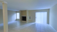This two-floor space offers a clean, functional layout with neutral tones throughout. The main living area is generously sized, finished with light-colored ceramic tile flooring that extends across the entire space, lending a cohesive and easy-to-maintain surface underfoot. The room is anchored by a built-in fireplace set into a structural column, accompanied by a recessed niche ideal for display or storage. The warm beige walls provide a neutral backdrop that complements a variety of décor styles. Natural light is a standout feature of this space, with a large sliding glass door dressed in vertical blinds dominating one wall and allowing abundant light to pour in. An additional window on the adjacent wall further brightens the interior. The open, unobstructed layout of the main living area offers flexibility for a range of furniture arrangements. With two floors, the property provides distinct separation between living and private spaces. The overall ambiance is bright, airy, and understated, offering a solid foundation for personalization.