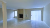 This two-floor space offers a clean, functional layout with neutral tones throughout. The main living area is generously sized, finished with light-colored ceramic tile flooring that extends across the entire space, lending a cohesive and easy-to-maintain surface underfoot. The room is anchored by a built-in fireplace set into a structural column, accompanied by a recessed niche ideal for display or storage. The warm beige walls provide a neutral backdrop that complements a variety of décor styles. Natural light is a standout feature of this space, with a large sliding glass door dressed in vertical blinds dominating one wall and allowing abundant light to pour in. An additional window on the adjacent wall further brightens the interior. The open, unobstructed layout of the main living area offers flexibility for a range of furniture arrangements. With two floors, the property provides distinct separation between living and private spaces. The overall ambiance is bright, airy, and understated, offering a solid foundation for personalization.