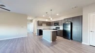 Located at 2101 Williamson Rd in Griffin, Georgia, this single-story residence offers a thoughtfully designed layout with modern finishes throughout. The open-concept kitchen serves as the heart of the home, showcasing rich dark wood cabinetry, light-toned countertops, and a full suite of black appliances including a refrigerator, range, and built-in microwave. A central kitchen island with pendant lighting overhead provides additional prep space and a natural gathering point that flows seamlessly into the living area. Light wood-style luxury vinyl flooring extends through the main living spaces, lending a clean, contemporary feel, while recessed lighting keeps the area bright and welcoming. The entry foyer features the same durable flooring and offers a clean, open transition into the living areas. Bedrooms are finished with plush carpeting and feature windows that allow natural light to fill the rooms. A spacious walk-in closet with wire shelving provides generous storage. The bathrooms are well-appointed with dark wood vanities, white countertops, large mirrors, and brushed nickel fixtures. A full tub-shower combo with clean white surrounds completes the bathroom. The overall design palette of warm neutrals and dark wood accents creates a cohesive, modern aesthetic throughout the home.