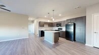 Located at 2101 Williamson Rd in Griffin, Georgia, this single-story residence offers a thoughtfully designed layout with modern finishes throughout. The open-concept kitchen serves as the heart of the home, showcasing rich dark wood cabinetry, light-toned countertops, and a full suite of black appliances including a refrigerator, range, and built-in microwave. A central kitchen island with pendant lighting overhead provides additional prep space and a natural gathering point that flows seamlessly into the living area. Light wood-style luxury vinyl flooring extends through the main living spaces, lending a clean, contemporary feel, while recessed lighting keeps the area bright and welcoming. The entry foyer features the same durable flooring and offers a clean, open transition into the living areas. Bedrooms are finished with plush carpeting and feature windows that allow natural light to fill the rooms. A spacious walk-in closet with wire shelving provides generous storage. The bathrooms are well-appointed with dark wood vanities, white countertops, large mirrors, and brushed nickel fixtures. A full tub-shower combo with clean white surrounds completes the bathroom. The overall design palette of warm neutrals and dark wood accents creates a cohesive, modern aesthetic throughout the home.