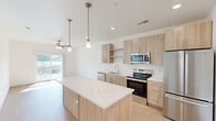 Located at 14801 Statesville Rd in Huntersville, NC, this single-floor unit offers a thoughtfully designed layout that maximizes functionality and comfort. The open-concept kitchen serves as the centerpiece of the home, showcasing light wood cabinetry, a striking marble-veined quartz island with pendant lighting overhead, and a full suite of stainless steel appliances including a refrigerator, range, microwave, and dishwasher. Light wood-tone flooring runs throughout the main living area, contributing to a bright, airy aesthetic. The bedroom is a generously sized retreat finished with soft carpet underfoot, crisp white walls, a ceiling fan, and a window that invites natural light and views of the surrounding greenery. A dedicated walk-in closet adjoins the bedroom, featuring multi-level wire shelving for ample storage. The bathroom is clean and functional, offering a full soaking tub and shower combination, a light wood vanity with a quartz countertop, and wood-look flooring that ties seamlessly to the rest of the home. Recessed lighting and a neutral white palette throughout the unit create a cohesive, modern atmosphere well-suited for comfortable everyday living.