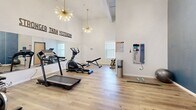 Located at 810 Monocacy St in Bethlehem, PA, this well-appointed exercise room delivers a thoughtfully designed fitness environment within a compact, single-floor layout. Soaring ceilings give the space an open, airy feel that defies its modest footprint, while a pair of striking gold sputnik chandeliers add a stylish, contemporary touch to the atmosphere.

The room features warm-toned luxury vinyl plank flooring throughout, providing a clean and durable surface ideal for a variety of workouts. Cardio equipment — including a treadmill, elliptical, and stationary bike — is arranged to maximize usability, complemented by a weight bench and a wall-mounted accessory rack stocked with resistance bands, yoga mats, and other fitness tools. A large floor-to-ceiling mirror along one wall enhances the sense of space and supports proper form during exercise.

A bold motivational phrase, "Stronger Than Yesterday," is prominently displayed along the upper wall, reinforcing an energetic and encouraging atmosphere. One accent wall features a deep blue textured finish that adds visual depth and contrast against the crisp white walls. Natural light filters in through a window, brightening the room during daytime use. The space is accessible via clearly marked entry and exit doors, making it both functional and user-friendly for daily fitness routines.