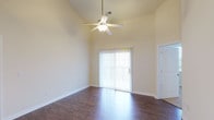 This two-floor residence offers a well-designed layout with a blend of practical finishes and comfortable living spaces. The main level centers around an open-concept kitchen and living area, where vaulted ceilings create a notably airy atmosphere. The kitchen is equipped with white raised-panel cabinetry, light countertops, stainless steel appliances including a refrigerator and range, and a peninsula that provides additional prep space and a natural divide between the kitchen and adjoining areas. Track lighting illuminates the kitchen, while tile flooring transitions to rich hardwood-style flooring in the living area. The living room benefits from soaring ceilings, a ceiling fan with light fixture, and a sliding glass door that invites natural light and provides outdoor access. Upstairs, the bedrooms feature plush carpeting and windows that bring in natural light. The bathroom includes a tiled tub and shower surround with light tile flooring, situated adjacent to a spacious walk-in closet outfitted with multi-level built-in shelving and hanging rods. A staircase with a white balustrade connects the two levels, adding a classic architectural detail to the interior.
