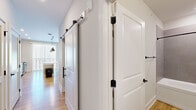 Located at 135 Ballentrae Ct in Chapel Hill, NC, this thoughtfully designed two-bedroom, one-bathroom home offers a cohesive modern aesthetic throughout its single floor. Warm hardwood flooring runs through the main living areas, complemented by clean white walls and black hardware accents that lend a contemporary feel.

The open-concept kitchen and dining area serves as the heart of the home, featuring gray shaker-style cabinetry extending to the ceiling, a white countertop island, subway tile backsplash, stainless steel appliances, and a trio of industrial-style pendant lights. Large windows with vertical blinds flood the space with natural light.

A hallway with stylish sliding barn doors provides access to the bedrooms and bathroom. The primary bedroom features hardwood flooring and a ceiling fan, while the second bedroom is finished with plush carpet, warm neutral tones, and closet access. Both rooms offer a calm, versatile atmosphere.

The bathroom is efficiently designed with wood-look flooring, a tiled tub-surround in soft gray, white cabinetry, and matte black fixtures that echo the home's consistent design language. Every detail of this Chapel Hill home reflects clean, modern craftsmanship suited for comfortable everyday living.