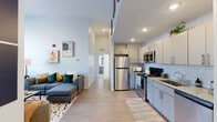 Located in the heart of Baltimore at 418 W Fayette St, this modern single-floor unit offers a thoughtfully designed open-concept layout that seamlessly connects the living, dining, and kitchen areas. Light-toned luxury vinyl plank flooring flows throughout the main living spaces, complemented by crisp white walls and recessed lighting that create a bright, airy atmosphere.

The kitchen is well-appointed with stainless steel appliances—including a refrigerator, range, and microwave—paired with granite countertops, a subway tile backsplash, and sleek gray cabinetry offering ample storage. The open living and dining area benefits from a large window overlooking the surrounding urban streetscape, filling the space with natural light. A ceiling fan adds comfort to the area.

The unit includes two bedrooms, each featuring plush carpeting and closet space. One bedroom enjoys a large corner window with views of the Baltimore cityscape. Both bathrooms are finished with granite-topped vanities, tile surround tub-shower combinations, and clean, contemporary fixtures.

The overall design aesthetic is clean and modern, with a neutral palette that provides a versatile backdrop suited for a variety of interior styles. The unit's central downtown Baltimore location places residents within close proximity to the city's cultural, dining, and business districts.