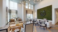 This single-floor amenity facility presents a thoughtfully designed community space that blends upscale aesthetics with practical functionality. The grand lobby immediately impresses with soaring double-height ceilings, an eye-catching cascading chandelier, and shiplap accent walls. A dramatic living moss wall art installation serves as a striking focal point near the reception desk, which features a distinctive marble-look surface. Floor-to-ceiling windows flood the space with natural light while offering outdoor views, and elegant patterned drapery adds a refined finishing touch. A comfortable lounge area with oversized armchairs and tranquil waterfront views provides an inviting retreat.

The community kitchen is a standout feature, anchored by a generous white quartz island with seating, dark navy cabinetry, a patterned tile backsplash, open wood shelving, and exposed wooden ceiling beams that add warmth and character. Large-format tile flooring grounds the space elegantly.

An airy dining room with soaring ceilings, bold circular pendant lighting, and black-framed French doors opening to an outdoor courtyard accommodates group gatherings with ease. The fitness center is well-equipped with cardio machines, free weights, exercise balls, and a full-length mirror wall, all bathed in natural light through frosted windows. Black-framed glass doors connect the amenity areas cohesively throughout.