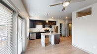 This studio in Baton Rouge, Louisiana offers a thoughtfully designed single-floor open-concept layout that efficiently combines living and kitchen areas into one cohesive space. Light wood-style flooring flows throughout, complementing the neutral, light-toned walls that lend a clean and modern aesthetic.

The kitchen is a standout feature, equipped with dark espresso cabinetry, stainless steel appliances including a refrigerator, range, microwave, and dishwasher, and granite countertops that extend across a central island. The island, illuminated by a stylish pendant light, provides both additional prep space and a casual dining surface. A ceiling fan overhead ensures comfortable airflow throughout the main living area.

Elevated clerestory windows are positioned above an interior wall, allowing natural light to filter into the living zone without sacrificing privacy. Large windows and a set of glass-paneled doors at the far end of the space invite additional daylight and provide views to the exterior.

A hallway connects to the bathroom, which features dark wood cabinetry with a granite-topped vanity, a tub-shower combination, and wood-style flooring consistent with the rest of the unit. A walk-in closet is accessible from the hallway, offering generous storage. Recessed lighting and ceiling fans throughout complete this functional and contemporary studio.