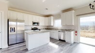 This newly constructed two-story home showcases contemporary finishes and thoughtful design throughout. The heart of the home is a spacious, well-appointed kitchen featuring crisp white shaker-style cabinetry extending to the ceiling, striking granite countertops with bold veining, and a full suite of stainless steel appliances including a gas range, over-the-range microwave, dishwasher, and refrigerator. A central kitchen island provides additional prep and storage space, while a subway tile backsplash and light gray wood-style flooring add modern character. Crown molding and recessed lighting elevate the overall aesthetic.

The bathrooms are finished to a high standard, with large-format gray tile covering the walls and floors. One bathroom features a sleek glass-enclosed walk-in shower with a built-in corner seat, while another offers a tub-shower combination, a white vanity with granite countertop, and a window that brings in natural light.

Additional rooms include generously sized bedrooms with neutral wall tones, crown molding, and large windows, as well as an attached garage with ample depth. Some areas of the home reflect active construction staging, indicating this is a new build nearing completion. The overall ambiance is clean, bright, and move-in ready.