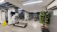Located at 295 Dufferin St in Toronto's vibrant King West neighbourhood, this fitness facility offers a comprehensive and well-organized space for a full range of workout activities. The facility spans a single floor and is divided into two distinct zones designed to accommodate various training styles.

The main exercise room features a polished concrete floor and is outfitted with a strong selection of cardio equipment, including treadmills and elliptical machines, each equipped with individual display monitors. Strength training stations and weight machines are thoughtfully arranged throughout the space, complemented by wall-mounted televisions and mirrors that enhance the open feel of the room. Exposed ductwork and industrial-style linear lighting run overhead, lending the space a modern, urban aesthetic. A small service station with a sink and informational signage adds a practical touch.

A secondary open training area provides ample room for functional fitness and group exercise. This zone features grey concrete block walls and is energized by a bold motivational mural with words like "CAPABLE" rendered in striking yellow and dark typography. Stability balls and fitness accessories are readily available, and a wall-mounted air conditioning unit ensures comfort year-round. Together, both areas create a versatile, well-lit fitness environment suited for a wide range of users and training needs.