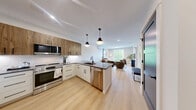 Located at 5205 Taylor Pond Ln in Billerica, MA, this well-appointed 2-bedroom, 2-bathroom residence offers a thoughtfully designed open-concept layout finished with light hardwood flooring and a crisp, neutral palette throughout. The kitchen is a standout feature, showcasing a two-tone design with white lower cabinets and warm wood upper cabinetry, dark quartz countertops, white subway tile backsplash, stainless steel appliances, and a large island with seating for three — ideal for dining and entertaining. Pendant lighting above the island adds a modern touch. The kitchen flows seamlessly into the living room, which is bathed in natural light from a full sliding glass door that opens to an outdoor view of lush greenery. The primary bedroom is generously sized, offering a tranquil retreat with light-filled windows and direct access to a closet. The second bedroom features dual windows with serene tree views and light hardwood floors. Both bathrooms are finished with clean, modern tile work — one featuring a walk-in tiled shower and warm wood vanity cabinetry with matte black hardware, and the other with a tiled shower and neutral stone-look tile flooring. Shaker-style interior doors with matte black hardware complete the contemporary aesthetic throughout.