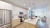 Located at 2418 Main St in Rocky Hill, CT, this thoughtfully designed one-bedroom, one-bathroom residence offers an efficient and stylish single-floor layout. Light wood-tone flooring flows throughout, creating a warm and cohesive aesthetic.

The open-concept kitchen is a standout feature, outfitted with stainless steel appliances including a French door refrigerator, electric range, and built-in microwave. Two-tone cabinetry pairs white upper cabinets with natural wood lower cabinets, complemented by crisp white countertops. A central island with an integrated sink and pendant lighting above adds both function and visual appeal.

The living room is bright and welcoming, with large windows and a glass-paneled door that invite abundant natural light. The bedroom offers a comfortable retreat with multiple windows, a ceiling fan, a distinctive geometric accent wall, and direct access to a full bathroom. The bathroom features a wood-toned vanity with a white countertop and wood-look tile flooring, and connects to a dedicated walk-in closet with full-width shelving and hanging rods. A stacked in-unit washer and dryer is also included. The clean, neutral palette and modern finishes throughout make this a refined and functional home.