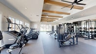 Located at 26 Mullein Dr in Hampstead, NC, this fitness center delivers a comprehensive workout facility designed with both function and aesthetics in mind. The single-floor exercise room is generously sized, offering an open, airy layout that accommodates a wide variety of training modalities without feeling crowded.

The interior design is defined by striking exposed wood ceiling beams set against crisp white walls and ceilings, creating a modern farmhouse aesthetic. Pendant lighting and large ceiling fans complement the abundant natural light that pours in through oversized windows and sliding glass doors. Durable rubber and epoxy flooring covers the workout areas, providing both safety and easy maintenance.

Equipment is thoughtfully arranged throughout the space and includes treadmills, ellipticals, a rowing machine, cable machines, a full power rack with free weights, adjustable benches, and various stability accessories. A wall of mirrors in the strength zone enhances the sense of depth and supports proper form during lifts. A water fountain is also conveniently located within the room.

Sliding glass doors open directly to a covered outdoor turf area equipped with training tires, a ping pong table, and views of a putting green and community pool beyond — seamlessly extending the fitness experience to the outdoors.