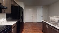 This single-story residence offers a cohesive design anchored by rich, dark hardwood-style flooring that extends throughout the main living areas, kitchen, and bathrooms. The open layout connects a well-appointed kitchen to a spacious living and dining area, both illuminated by a combination of ceiling fans with integrated lighting and a decorative chandelier. Windows fitted with horizontal blinds allow natural light to filter in throughout.

The kitchen is equipped with dark espresso-toned cabinetry extending to the upper walls, granite-style countertops, and a full suite of black appliances including a side-by-side refrigerator with ice and water dispenser, electric range, microwave, and dishwasher. A pantry or closet door is conveniently located adjacent to the main entry.

Bedrooms feature plush neutral carpet, ceiling fans, and blinds-covered windows that bring in natural light. The bathrooms are finished with the same dark cabinetry, granite-style countertops, large mirrors, and wood-look flooring. One bathroom includes a tub-shower combination, while a second offers a single-vanity layout with bright overhead lighting. The overall aesthetic is consistent and modern throughout.