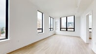 Located at 4909 Auburn Ave in the heart of Bethesda, MD, this well-appointed 2-bedroom, 2-bathroom unit offers a clean, contemporary aesthetic throughout. Light wood flooring flows seamlessly across the entire living space, complementing the bright white walls and modern finishes that define the interior.

The open kitchen is outfitted with warm wood cabinetry, white quartz countertops, and stainless steel appliances, including a built-in oven, microwave, and dishwasher. A sliding glass door leads directly from the kitchen to a spacious rooftop terrace, complete with raised planters, young trees, and sweeping views of the Bethesda skyline.

The living area is bathed in natural light, courtesy of expansive floor-to-ceiling windows framed in sleek black — a design detail that carries throughout the unit. Built-in shelving adds a functional architectural touch to the living space.

The primary bedroom is generously sized, featuring multiple large windows that frame elevated city views. The second bedroom is equally bright, with its own window overlooking the surrounding urban landscape. Three closets provide ample storage throughout the unit.

Both bathrooms are thoughtfully finished, with the full bath showcasing marble-style tile surround, a soaking tub, and warm wood vanity cabinetry with clean white countertops.