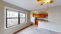 Situated at 6104 S Woodlawn Ave in Chicago's Woodlawn neighborhood, this single-floor residence offers a functional and well-organized layout. The open-concept living and kitchen area is bright and inviting, with large windows that frame views of the surrounding urban landscape and allow generous natural light to fill the space. Ceiling fans are present throughout, providing year-round air circulation. The kitchen is equipped with warm honey-toned wood cabinetry, granite-style countertops, a gas range, and a refrigerator. A peninsula counter seamlessly connects the kitchen to the living area, making it ideal for casual dining or meal prep. Tile flooring grounds the kitchen zone, while plush carpeting extends through the living and bedroom areas for added comfort. The bedroom features a ceiling fan, a radiator for supplemental heating, and a window with neighborhood views, with direct access to the bathroom. A spacious walk-in closet with wire shelving and hanging rods provides ample storage. The bathroom includes a full tub-shower combination with white tile surround, a vanity, a radiator, and a privacy window, rounding out this practical and comfortable Chicago residence.