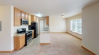 Located at 6801 S 133rd St in Seattle, WA, this single-floor unit offers a well-organized layout designed for comfortable everyday living. The open-concept kitchen and living area form the heart of the space, with the kitchen featuring warm honey-toned cabinetry, a central peninsula with counter seating, stainless steel appliances including a range, microwave, and refrigerator, and durable tile flooring. The kitchen flows seamlessly into the spacious carpeted living area, which is filled with natural light from a large window and a sliding glass door that opens onto a private balcony with tree views. A tile-surround corner fireplace serves as a standout focal point in the living room, adding warmth and character. The bedrooms are generously sized, finished with plush wall-to-wall carpeting, warm neutral walls, and windows fitted with blinds. A baseboard heating unit in the bedroom ensures year-round comfort. The bathroom is thoughtfully appointed with a full tub-shower combination, white tile surround, a wood-toned vanity with an integrated sink, and earthy tile flooring. Throughout the unit, warm beige tones, wood-accented baseboards, and consistent finishes create a cohesive and inviting atmosphere.