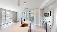 Located at 8781 Georgia Ave in Silver Spring, MD, this modern single-floor residence offers three bedrooms and three bathrooms thoughtfully arranged for comfortable living. The open-concept kitchen and living area serves as the heart of the home, featuring a sleek island with a white quartz countertop and a matte black undermount sink, complemented by flat-front gray cabinetry and stainless steel appliances including a refrigerator, range, and built-in microwave. Pendant lighting and recessed fixtures illuminate the space, while large sliding glass doors open to an outdoor balcony and invite generous natural light. Light wood-tone flooring flows seamlessly throughout the entire residence, enhancing the bright, airy atmosphere. Each of the three bedrooms offers ample proportions, large windows with views of surrounding greenery, and neutral-toned walls that provide a calm, versatile backdrop. The primary bedroom is well-sized and sun-drenched. The three bathrooms are finished with marble-look tile flooring, white vanities, and matte black hardware accents. One bathroom features a glass-enclosed walk-in shower with white subway tile, adding a refined, contemporary touch. Clean lines, neutral finishes, and abundant natural light define the overall ambiance of this well-designed residence.
