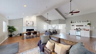 Located at 314 Great Lakes Dr in Noblesville, Indiana, this single-floor space offers an open-concept layout that seamlessly integrates a living room, dining area, and kitchen. The most striking architectural feature is the dramatic vaulted ceiling, which soars overhead and lends a grand sense of volume throughout the main area. Warm hardwood flooring runs continuously underfoot, unifying the space with a cohesive, inviting feel.

The living area is anchored by a classic brick fireplace with a clean white finish, serving as a focal point beneath the high ceiling. Ceiling fans provide both function and style, complementing the abundant natural light that pours in through multiple windows. A comfortable seating arrangement and designated dining space with a wood table and leather chairs make the layout highly functional.

A standout feature is the built-in coffee bar station, complete with white cabinetry, granite-style countertops, open shelving, and a beverage refrigerator — an ideal amenity for a shared or community space. The kitchen features white shaker cabinets, granite-look countertops, and a large window that fills the room with natural light. An elegant arched entryway adds a refined architectural detail, while the neutral gray walls throughout create a calm, modern backdrop that ties every element of the space together.