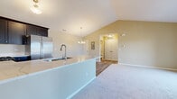Located at 506 Timber Pointe Dr in Joliet, Illinois, this single-story home showcases a thoughtfully designed open-concept layout that seamlessly connects the kitchen, dining, and living areas. Soaring vaulted ceilings with warm neutral tones create an airy, spacious atmosphere throughout the main living space. The kitchen is well-appointed with dark espresso cabinetry, stainless steel appliances including a refrigerator, range, and microwave, and a peninsula countertop with an integrated sink — ideal for both cooking and casual entertaining. Light hardwood-style flooring runs through the kitchen and dining area, while plush carpeting extends into the living room and bedrooms, adding warmth underfoot. A chandelier provides an elegant focal point above the dining space. The bedrooms are generously sized, featuring vaulted or elevated ceilings, large windows that invite natural light, and views of the surrounding neighborhood. One bedroom offers direct access to a private balcony through a sliding glass door, extending the living space outdoors. The bathroom is clean and functional, featuring a full tub and shower combination with chrome fixtures. Double doors in the main living area lead to additional interior spaces, completing this well-organized and move-in-ready home.