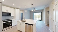 Located in Bonita Springs, FL, this well-appointed 2-bedroom, 2-bathroom residence offers a thoughtfully designed single-floor layout. The open-concept kitchen serves as the heart of the home, showcasing crisp white cabinetry, a light blue tile backsplash, quartz countertops, and a central island with an undermount sink. Stainless steel appliances — including a French door refrigerator, range, microwave, and dishwasher — complete the modern kitchen. Warm wood-look flooring flows throughout the main living areas, while recessed and pendant lighting add a polished touch. Sliding glass doors in the living area lead to a private patio, allowing for natural light and outdoor views of the surrounding Florida landscape. The spacious primary bedroom features a ceiling fan, large windows, and direct patio access, complemented by an en-suite bathroom with a glass-enclosed shower, white vanity, and a walk-in closet with wire shelving. The second bedroom is finished with plush carpeting and a closet. A dedicated hallway, additional closets, and an in-unit laundry area add to the home's practical functionality. The overall aesthetic is clean, bright, and move-in ready.